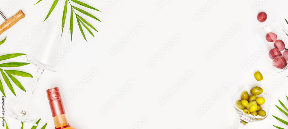 Food banner with an empty wine glass, bottle of rose wine, green olives, grapes and palm leaves on a white background with copy space. The concept of a tropical holiday resort and relax. Summer party Food banner with an empty wine glass, bottle of rose wine, green olives, grapes and palm leaves on a white background with copy space. The concept of a tropical holiday resort and relax. Summer party