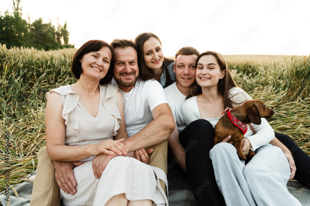 large family with five people sits in a wheat field at sunset of the day. happy family hugs while on a picnic. family vacation for parents with children