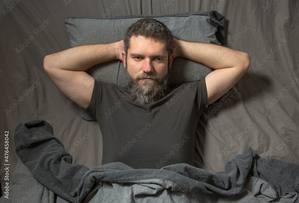 a gray-haired young man with a beard lies in bed at night and thinks. The concept of insomnia.. a gray-haired young man with a beard lies in bed at night and thinks. The concept of insomnia..