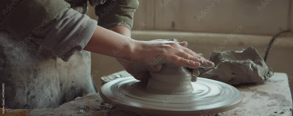 Close up shot of female potter shaping clay on spinning wheel with wet hands while making ceramics in workshop Close up shot of female potter shaping clay on spinning wheel with wet hands while making ceramics in workshop