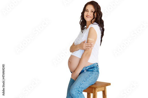 Vaccinated pregnant woman shows a plaster cast on her arm after an injection of Covid-19 vaccine, cheerful sits on a white background. Coronavirus vaccination campaign.