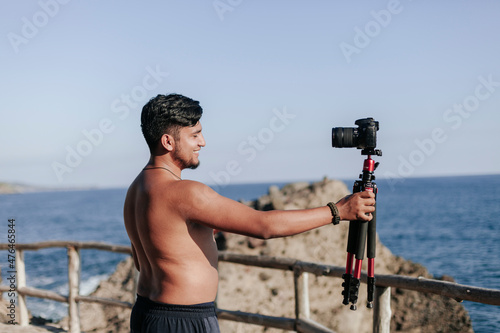 hombre joven sin camisa grabando video en la playa