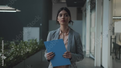 Portrait of business woman walking on meeting in office corridor, carrying folder with business documents, follow shott photo