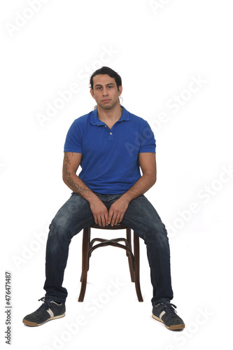 front view of man with ponytail and casual clothing and tattoos sitting a chair on white background