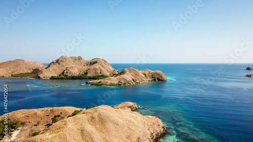 A drone shot of two bigger paradise islands in Komodo National Park, Flores, Indonesia. The islands have scarcely any trees and bushes. Dry land. Idyllic white sand beaches. Island hoping