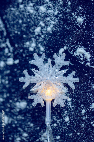 Snowflake shaped Christmas light on a snowy blue background.