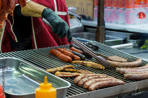 Fotografia Man with gloves grilling sausages, chorizo, bacon and black pudding on barbecue