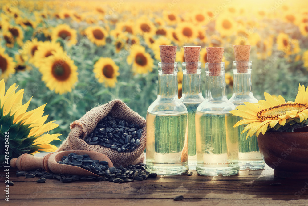Φωτογραφία Three bottles of sunflower oil and bag of black sunflower seeds, beautiful yellow sunflower field on background