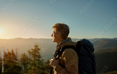 Obraz na plátně Side view man traveler with backpack standing tanding in sunset light among moun