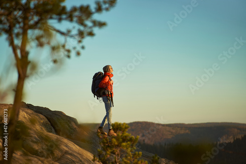 Tourist woman enjoying nature and looking confident and happy with her hiking expedition outdoors on top of mountain at sunset.