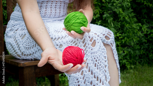 Manos de mujer sosteniendo ovillos de lana rojo y verde con vestido de crochet blanco