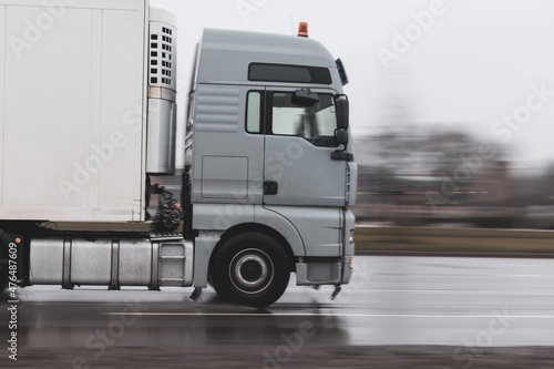 A gray truck in the rain pulls a semi-trailer on wet asphalt close-up. Motion blur