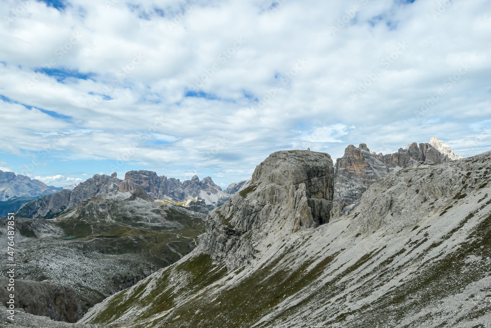 A panoramic view on a valley in Italian Dolomites. There is a massive mountain in front, with very steep and sharp slopes. In the back there are smaller mountain chains. Raw and desolated landscape