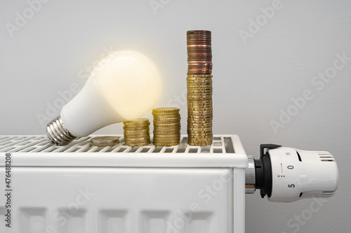 Energy crisis. White LED light bulb on a radiator with money coin stack. Growing electric and gas bill. Central heating.