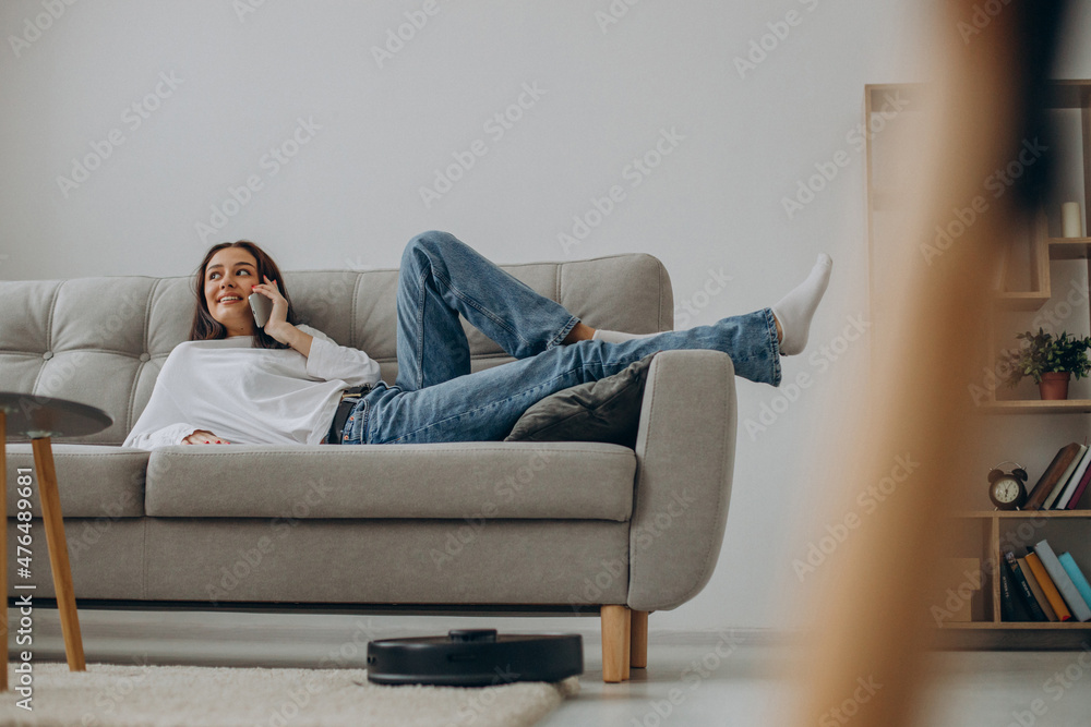 Woman using phone while robot vacuum cleaner cleaning up the room Woman using phone while robot vacuum cleaner cleaning up the room