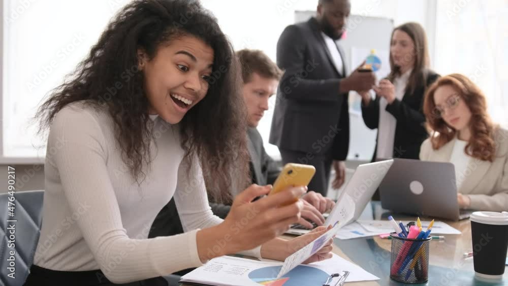 A corporate employee in the office rejoices at a successful deal using an app on her smartphone. Excited business woman sit at desk look at smartphone feel euphoric overjoyed A corporate employee in the office rejoices at a successful deal using an app on her smartphone. Excited business woman sit at desk look at smartphone feel euphoric overjoyed
