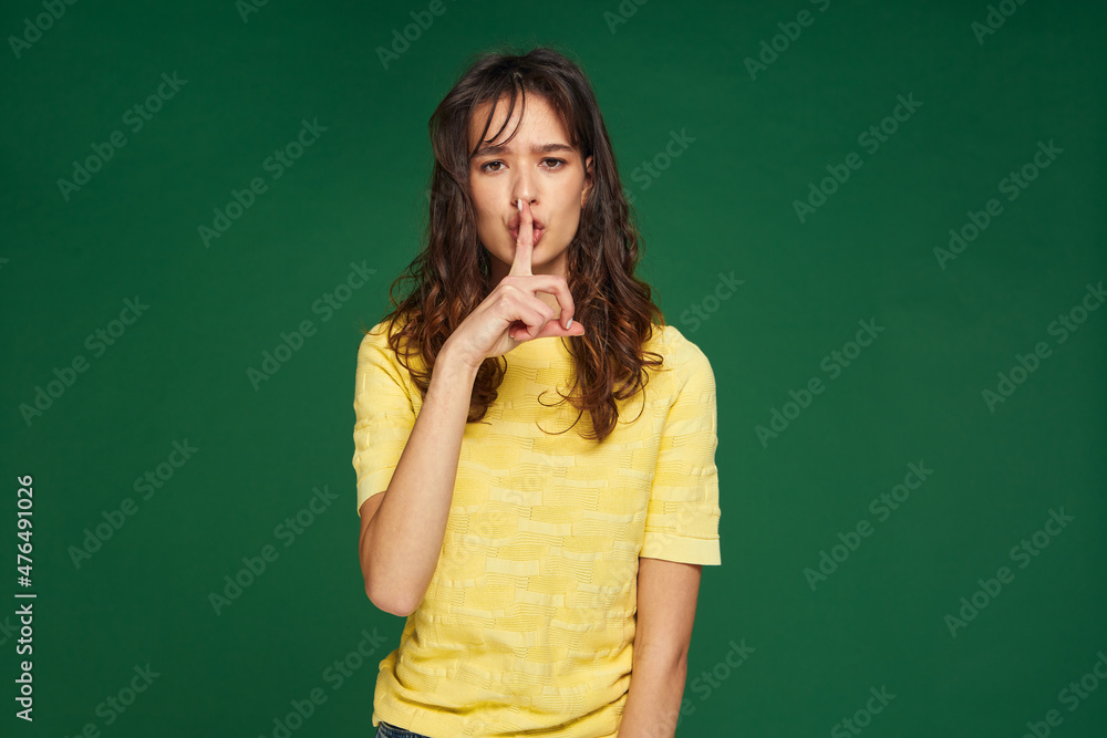 Serious young girl show silence gesture to keep secret private information on green studio background. Privacy concept Serious young girl show silence gesture to keep secret private information on green studio background. Privacy concept