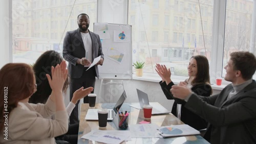 African American coach presents for company members financial report standing near whiteboard where shown sales statistics in graphs. Confident company owner teach interns acquaints with nuances of