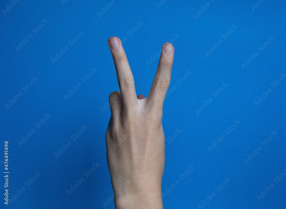 Finger gesture two fingers - peace, dude, victory, on a blue background Finger gesture two fingers - peace, dude, victory, on a blue background