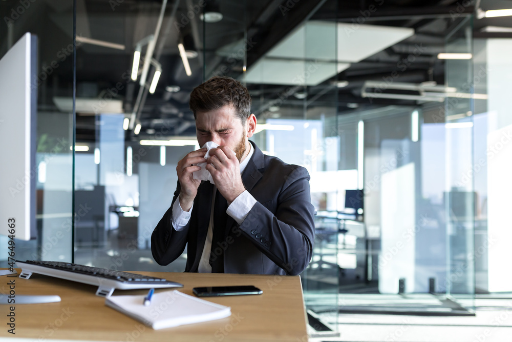 A man with a runny nose and fever works in the office, a sick businessman at the computer has a runny nose A man with a runny nose and fever works in the office, a sick businessman at the computer has a runny nose