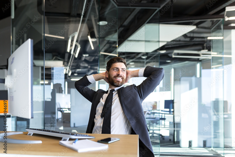 Happy and dreamy businessman, resting at work with his hands behind his head, working in a modern office at the computer Happy and dreamy businessman, resting at work with his hands behind his head, working in a modern office at the computer