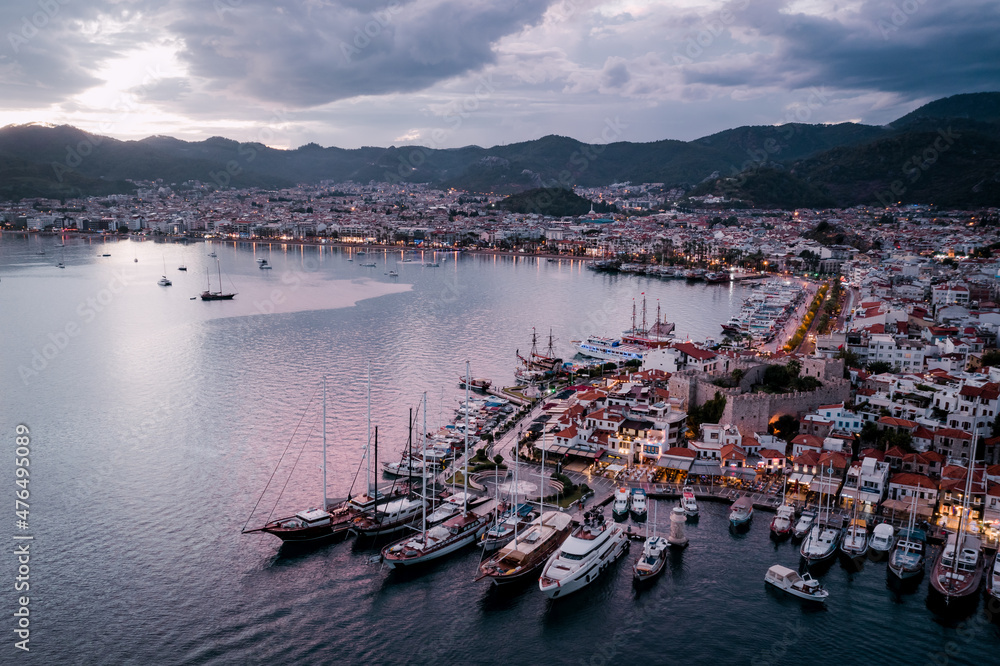 Aerial view of Marmaris harbor with yacht and sailboat with evening lighting. Colorful landscape of the night Turkish city. Beautiful sky at sunset
