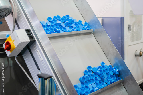 Many blue plastic bottle caps moving on conveyor belt of automatic compression molding machine at factory, exhibition: production line. Manufacturing, recycling, industry, technology equipment concept photo