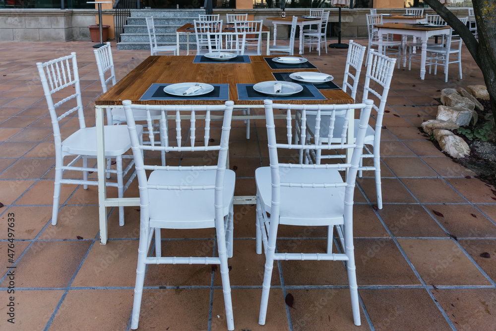 Front image of a wooden terrace table with 8 white chairs around it ready to eat.
