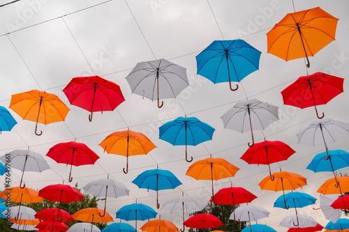 Colorful umbrellas hanging against gray overcast sky and swaying in wind at summer city festival - low angle view. Street decoration  celebration  art  holiday concept