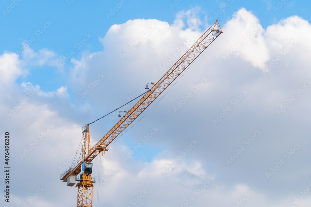 Yellow tower construction crane against summer cloudy sky with white clouds. Building process, architecture, urban, engineering, industrial and development concept