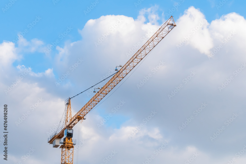 Yellow tower construction crane against summer cloudy sky with white clouds. Building process, architecture, urban, engineering, industrial and development concept Yellow tower construction crane against summer cloudy sky with white clouds. Building process, architecture, urban, engineering, industrial and development concept