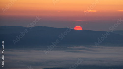 Wstające słonce znad górskich szczytów we mgle  / The rising sun over the mountain peaks in the fog