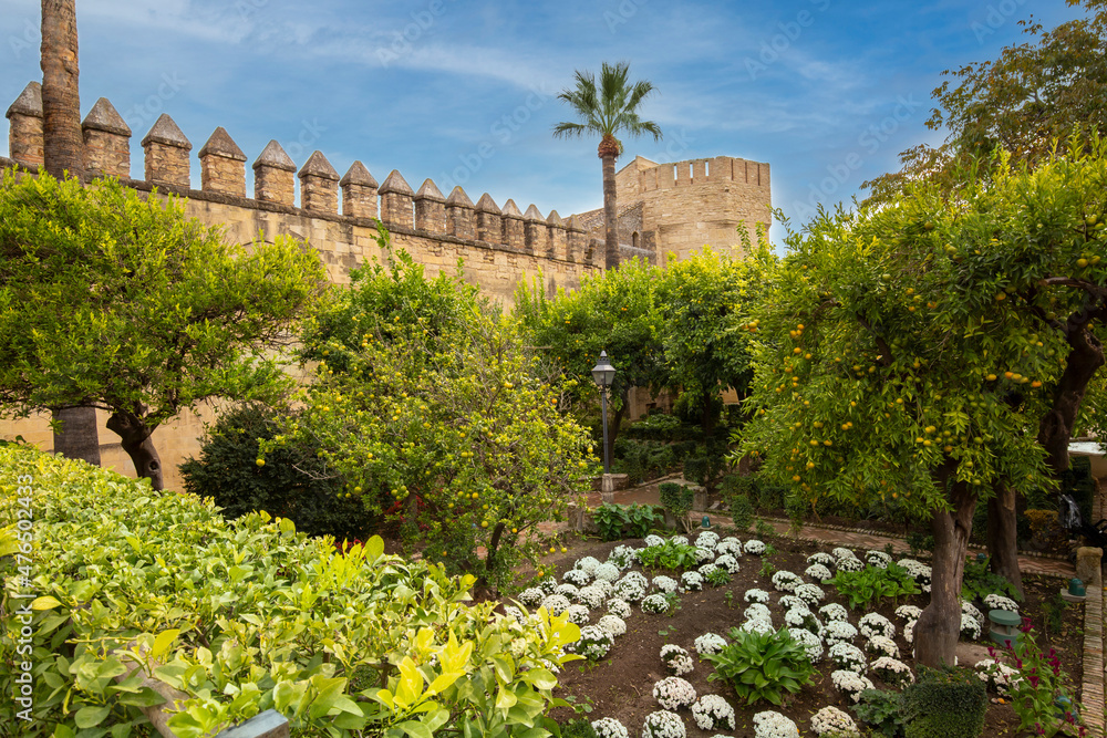 Gardens at the Alcazar de los Reyes Cristianos in Cordoba, Spain. Part of a stone wall and a tower surrounded by fruit trees and flowers