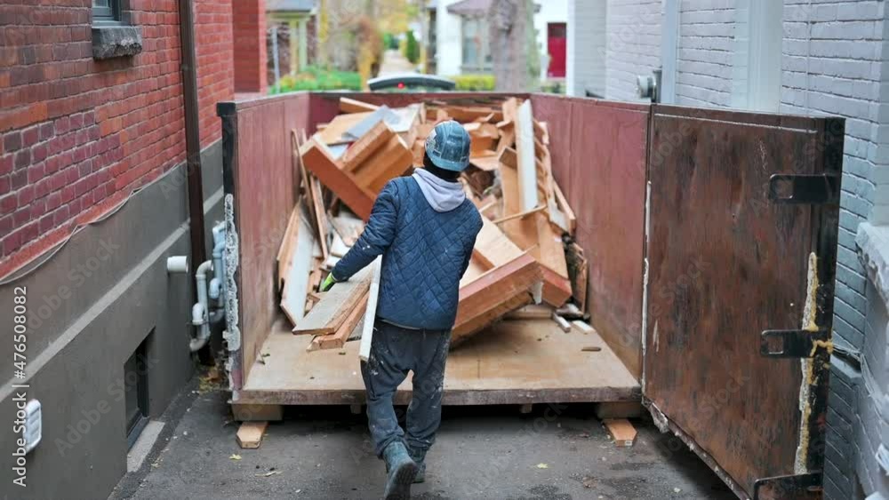 Construction labourer throwing out insulation into disposal bin Construction labourer throwing out insulation into disposal bin