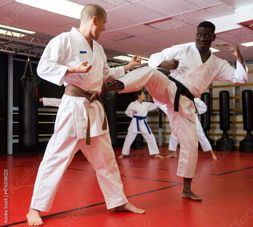 African-american and European men in kimono sparring together during group karate training in gym. Women sparring in background.
