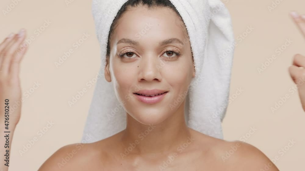 Good-looking young slim African American woman with a towel on her head and bare shoulders stokes her nose and cheeks smiling wide for the camera on beige background | Face care concept Good-looking young slim African American woman with a towel on her head and bare shoulders stokes her nose and cheeks smiling wide for the camera on beige background | Face care concept