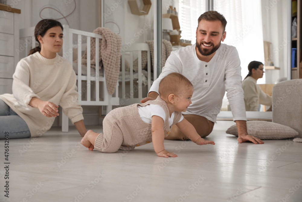Happy parents watching their baby crawl on floor at home Happy parents watching their baby crawl on floor at home