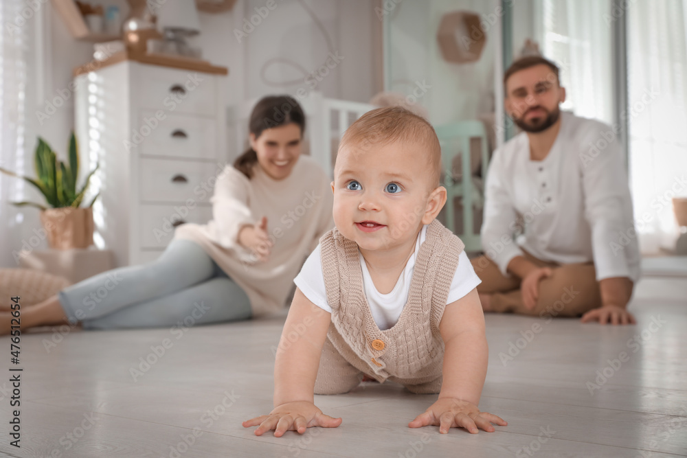 Happy parents watching their baby crawl on floor at home Happy parents watching their baby crawl on floor at home