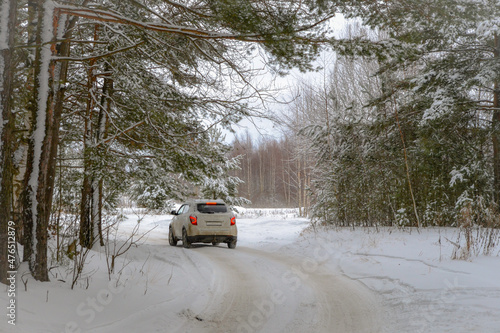 A fabulous trip in a small white car along a snow-white rural road in a winter forest among coniferous trees covered with snow