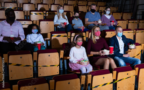 Adults with children wearing protective masks watching movie in cinema. Concept of precautions during coronavirus pandemic
