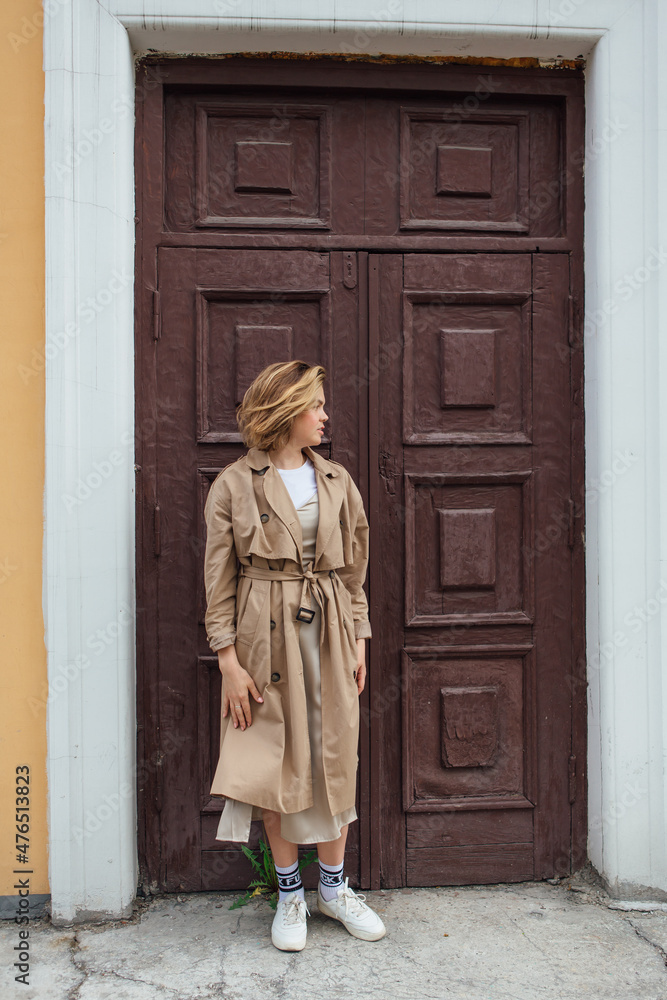 Young millennial woman with wild hair dressed in an autumn coat posing near the door of an old building.