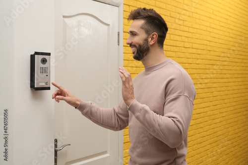 Happy man ringing intercom while waving to camera in entryway