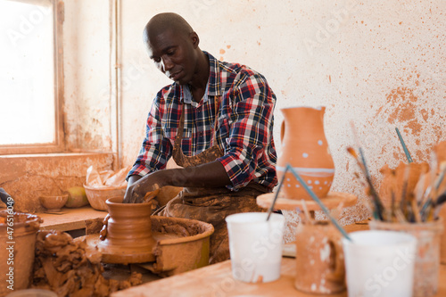 Skilled african american potter working on potters wheel making clay products in pottery workshop