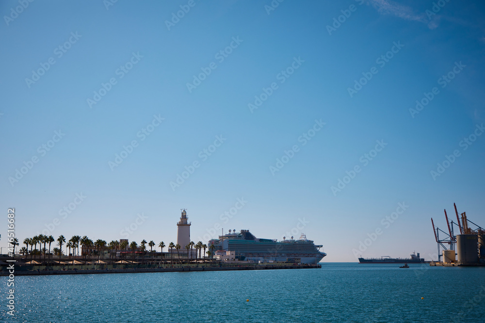 Lighthouse on the coast of Malaga in Spain with palm trees in front, boats and the Mediterranean sea