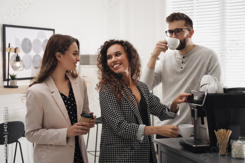 Fotografering African American woman talking with colleagues while using modern coffee machine