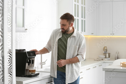 Young man preparing fresh aromatic coffee with modern machine in kitchen