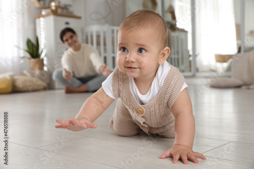 Happy mother watching her cute baby crawl on floor at home
