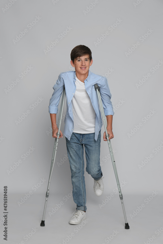 Teenage boy with injured leg using crutches on grey background Teenage boy with injured leg using crutches on grey background