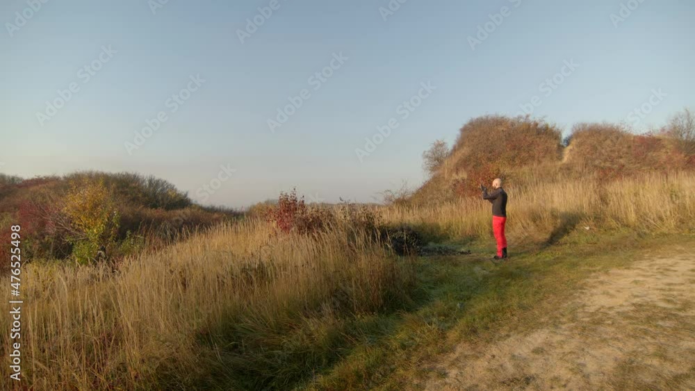 View of mid-adult man taking a picture while jogging and continues to run down the road. Sunny autumn morning. Clear blue sky on the background. View of mid-adult man taking a picture while jogging and continues to run down the road. Sunny autumn morning. Clear blue sky on the background.