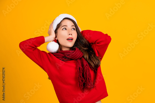 Shocked beautiful Asian girl wearing christmas hat isolated on yellow background. She covered both ears with her hands. © PBXStudio
